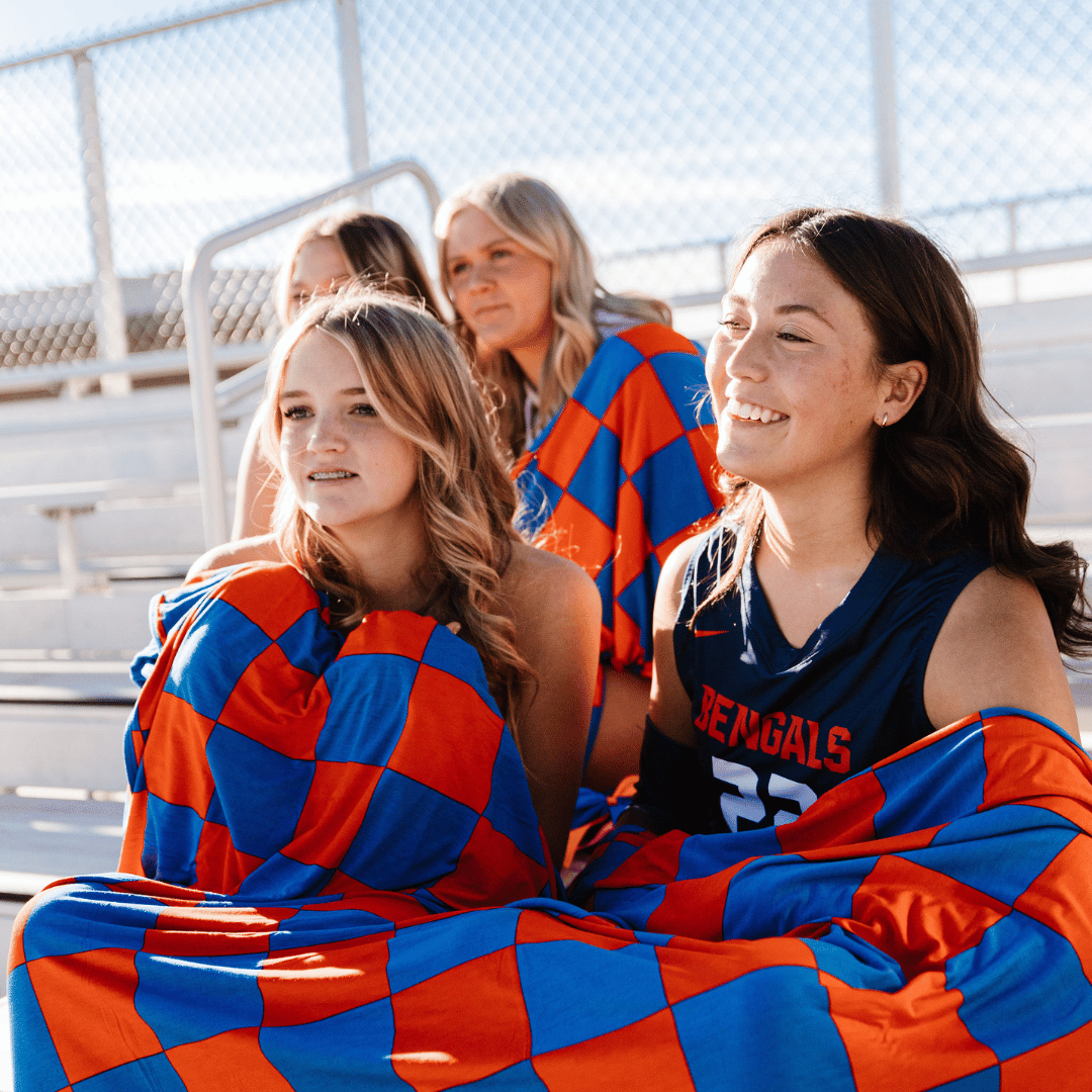 These girls are staying cozy in the stands with their Pipermoon blankets in their high school orange and blue colors.